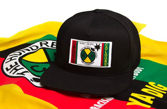 Black Cross Colours hat with vibrant logo, 90's fashion icon, on colorful fabric background.