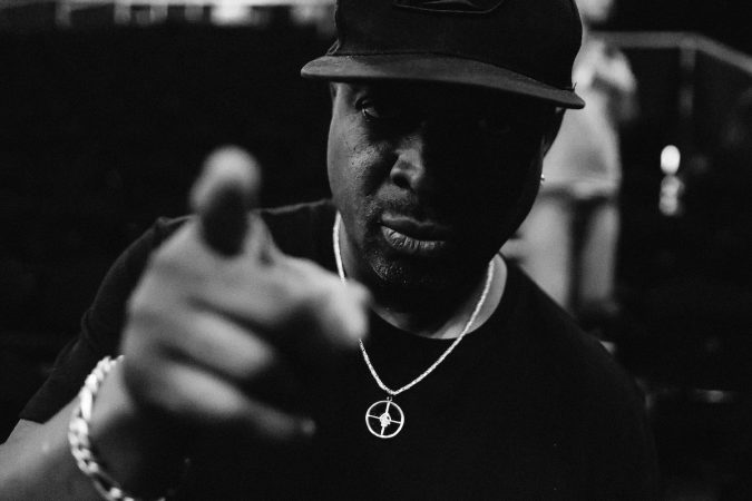Dynamic rapper and MC wearing a cap, pointing towards the camera, showcasing confidence and success.