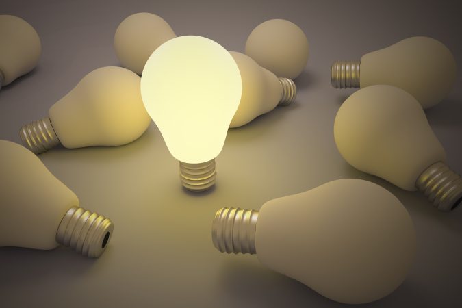 Illuminated light bulb among unlit bulbs symbolizing innovative ideas and productivity.