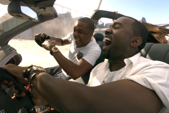Kanye West and Jay-Z laughing and having fun in a convertible car.